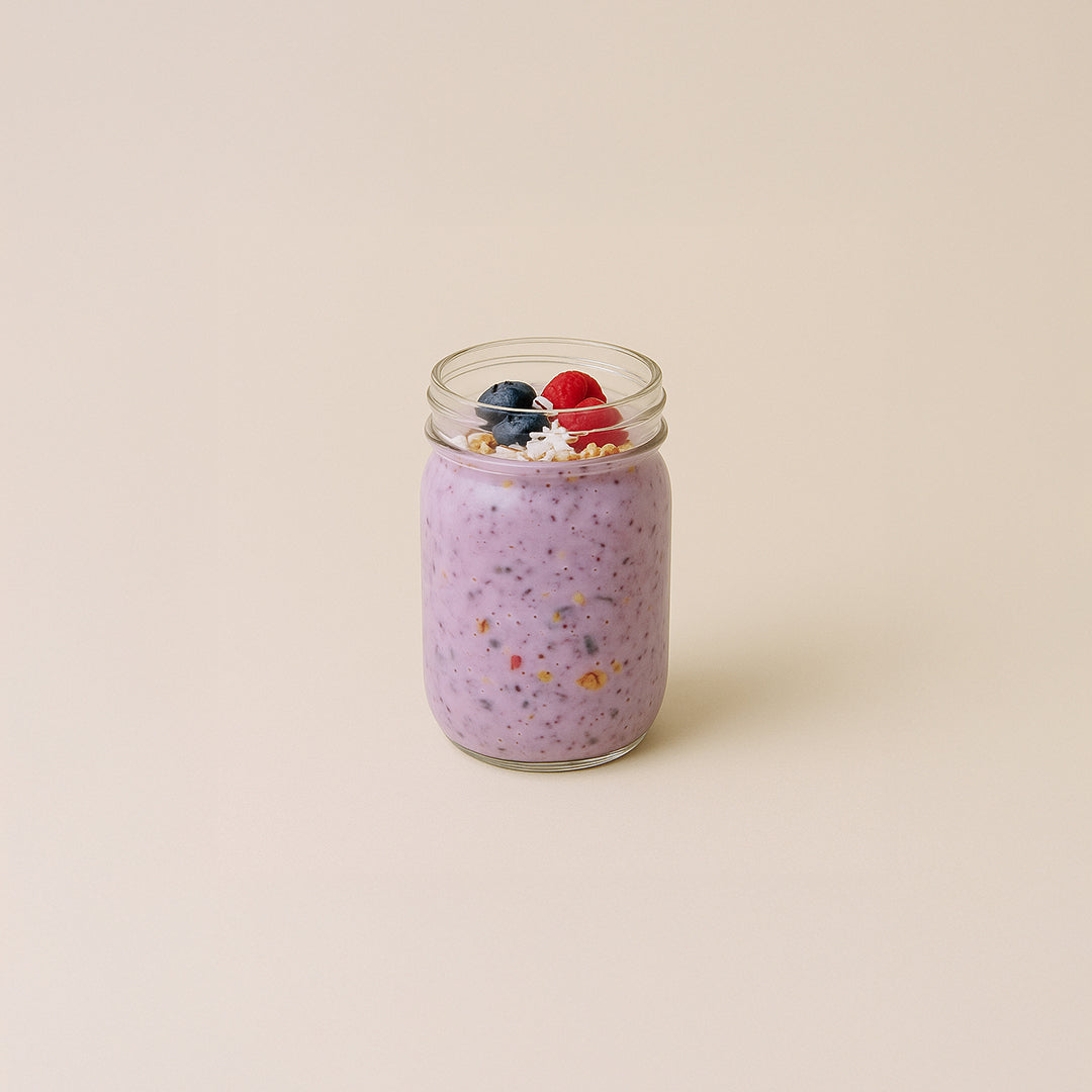 pot en verre rempli d’overnight oats mauve aux graines de chia, garni de framboises, bleuets et granola croquant