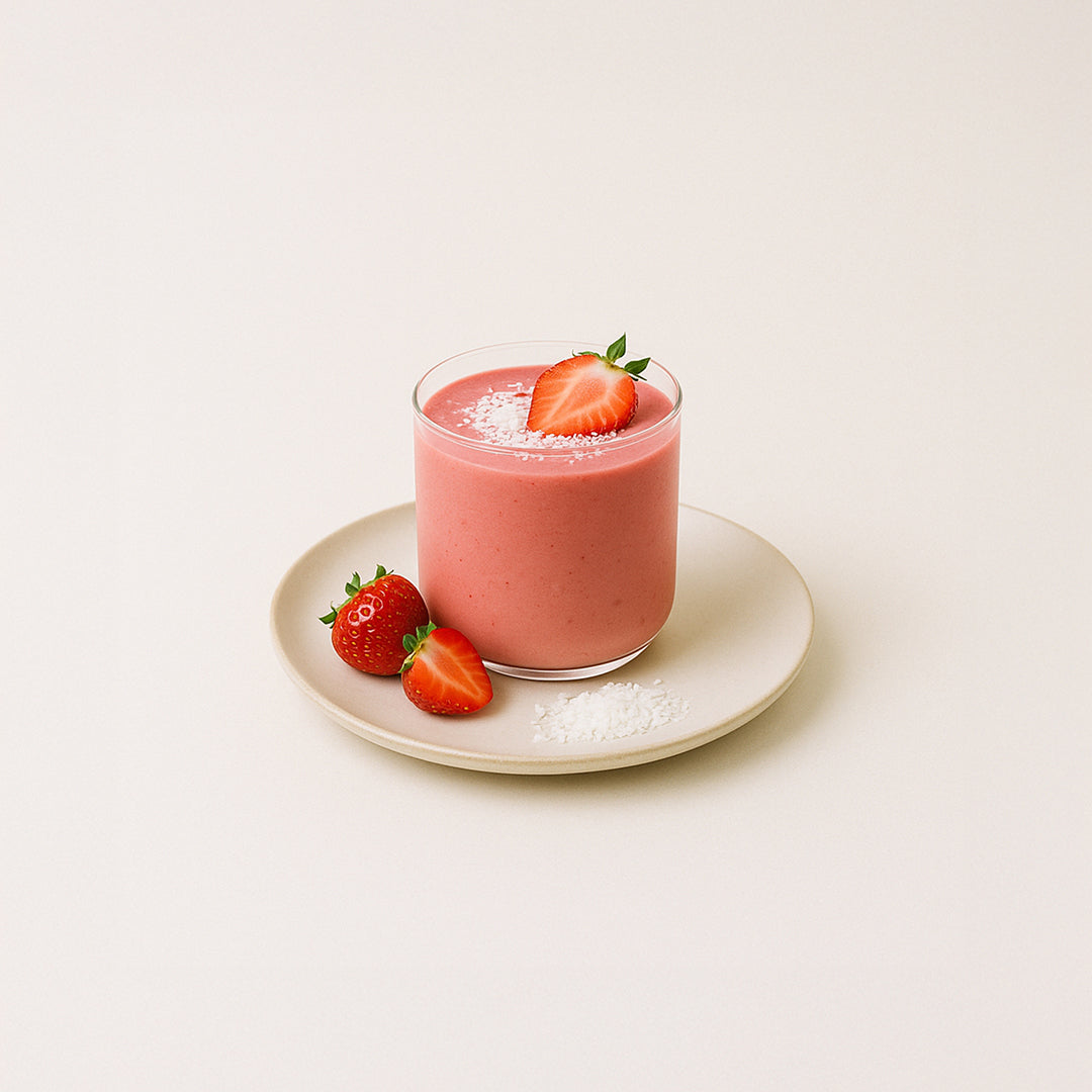 Smoothie rose aux fraises et bleuets enrichi en collagène marin, servi dans un verre transparent avec fraises fraîches et copeaux de noix de coco en garniture.